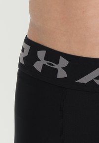 Black compression shorts with a thick waistband featuring a gray Under Armour logo. Fabric texture is smooth with slight sheen.