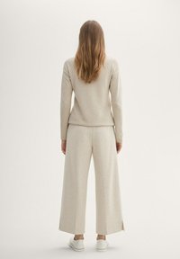 Ljusbeige tröja med ett texturerat mönster, ihop med vida beige byxor. Skorna är vita med en enkel design.