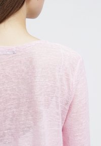 Ljust rosa, genomskinlig stickad topp med en enkel rund halsringning och en avslappnad passform. Mjuk textur med en något lös väv.