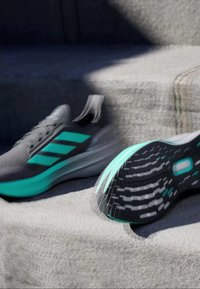 Athletic shoes with gray upper, teal accents, and three black stripes. Features include a sleek design and textured rubber outsole.