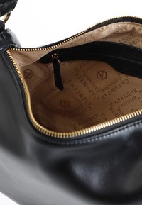 Borsa a tracolla in pelle nera con una cerniera dorata, interno foderato con tessuto beige e un motivo a logo ripetuto. Include una tasca interna con cerniera.