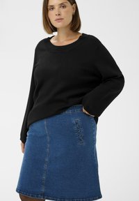 Black knit sweater with wide neckline and long sleeves, paired with a blue denim A-line skirt featuring a side pocket and stitch details.