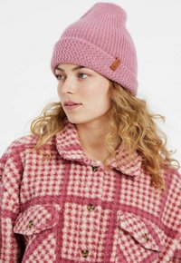 Berretto lavorato a maglia rosa con un design a coste testurizzate e un orlo pieghevole. Abbinato a una camicia in pile rosa e bianca a scacchi con bottoni.