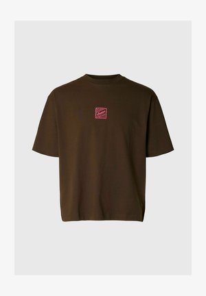 Temno rjava majica s kratkimi rokavi z majhnim rdečim kvadratnim logotipom s stilizirano napisom na sredini prsnega koša, enobarvno ozadje.