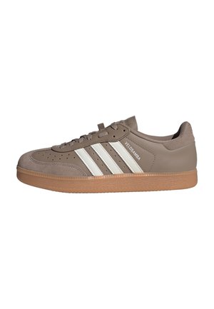 Taupekleurige lage sneaker met witte strepen, een rubberen zool, bovenwerk van suède en leer, en de tekst "VELOSAMBA" aan de zijkant.