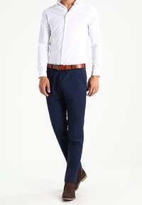 Witte overhemd met knopen, marineblauwe broek, leren bruine riem, bruine enkelboots; gladde stof, op maat gemaakte pasvorm, eenvoudig ontwerp, professionele uitstraling.