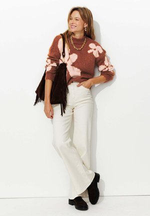Pull en tricot couleur rouille avec un motif floral rose, pantalon blanc taille haute évasé, sac à main en suédine marron avec des franges, et bottes à plateforme noires.