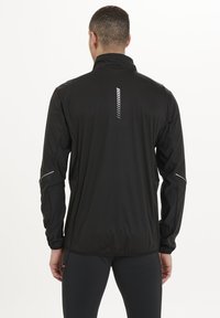 Schwarze Sportjacke mit hohem Kragen, reflektierenden Akzenten, Reißverschlusstaschen und vertikalem Streifenmuster auf dem Rücken. Leichtgewichtig, taillierte Passform.