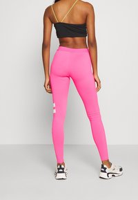 Różowe legginsy o dopasowanym kroju, wykonane z elastycznego materiału. Posiadają białe akcenty logo na lewej łydce. W połączeniu z beżowymi trampkami.