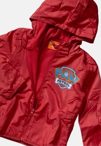 Czerwona kurtka przeciwwiatrowa z kapturem, wyposażona w polarowe podszycie oraz logo "Paw Patrol" na klatce piersiowej. Zamek błyskawiczny i długie rękawy.