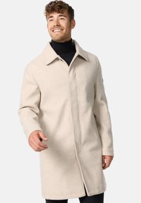 Beige uld-blend frakke med en struktureret design, spidse krave, skjult frontlynlås og to sidelommer, der har en glat tekstur.