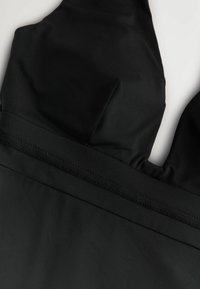 Zwart zwemkleding met een gladde, licht gestructureerde afwerking. Heeft een gestructureerde top met gevormde cups en een brede, platte tailleband.