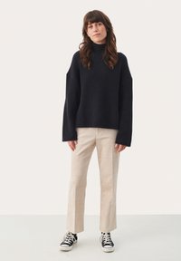 Pulover turtleneck cu jerseu ribat din navy închis, cu mâneci ample, asociat cu pantaloni din catifea ușoară de culoare bej și adidași negri din pânză. Design simplu.