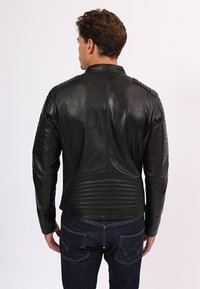 Giubbotto da motociclista in pelle nera con dettagli a coste sulle spalle e sulla schiena, taglio slim e una texture liscia. Presenta cuciture e cerniere a vista.