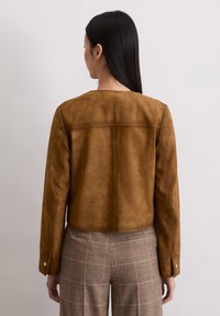 Braune Wildleder-Cropped-Jacke mit langen Ärmeln, glatter Textur und runder Ausschnitt. Der Rücken verfügt über eine horizontale Nahtdetails.