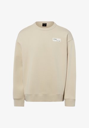 Beżowa bluza z długim rękawem i okrągłym dekoltem, z prążkowanymi ściągaczami przy mankietach i dole oraz małą białą prostokątną naszywką z logo na górnej części piersi.