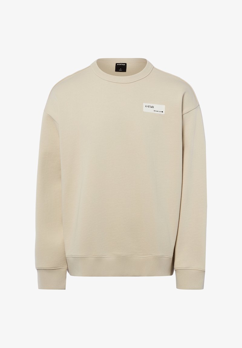 Beiger Sweatshirt mit Rundhalsausschnitt, langen Ärmeln, gerippten Bündchen und Saum sowie einem kleinen rechteckigen weißen Logo-Patch auf der oberen Brust.