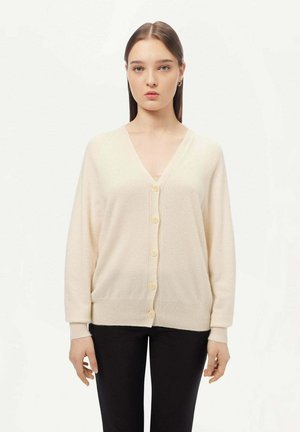 Helle cardigan in Cremfarbe mit V-Ausschnitt, gerippter Textur und sechs Knöpfen auf der Vorderseite. Lange Ärmel, lockerer Schnitt und weiches Strickmaterial.