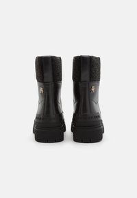 Stivaletti neri in pelle con un collare in tessuto grigio texture, suola nera spessa e un logo dorato sul tallone.