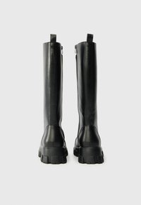 Μαύρες μπότες μέχρι το γόνατο με λείο δερμάτινο άνω μέρος, χοντρή ελαστική σόλα και κλείσιμο με φερμουάρ στο πίσω μέρος. Διαθέτουν υφασμένη τακούνι και θηλιά για να τις φορέσετε.