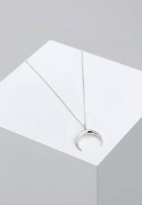 Collana d'argento con un pendente a forma di mezzaluna. Il pendente ha una finitura lucida e una catena sottile, poggiato su un'esposizione geometrica.
