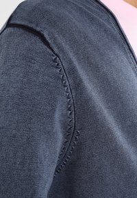 Dunkelblaue Strickjacke mit V-Ausschnitt, strukturierten Nähten an den Schultern und einer glatten Oberfläche.