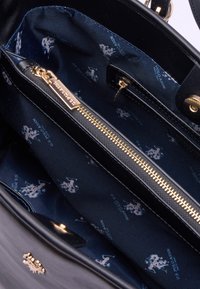 Interno di una borsa in pelle nera con una fodera blu navy caratterizzata da motivi logo ripetuti in azzurro chiaro, una cerniera dorata e dettagli hardware coordinati.