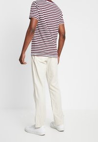 Camiseta de rayas granate y blanca combinada con pantalones beige claro y zapatillas blancas. La camiseta tiene un cuello redondo clásico y mangas cortas.