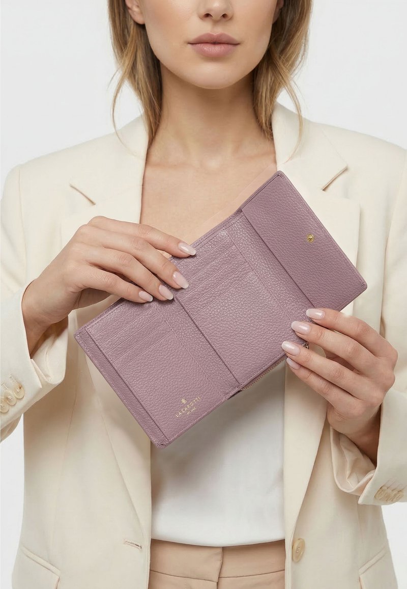 Donna con blazer beige che tiene in mano un portafoglio in pelle color malva aperto che mostra gli scomparti per le carte.