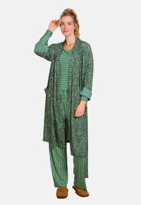 Groene bloemenbadjas met zakken over een groen gestreept shirt en broek. Zachte stof; ontspannen pasvorm. Bruine slippers maken de outfit compleet.