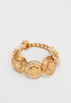 Bracciale in oro con charm circolari raffiguranti motivi leone, decorato con cristalli e intricati motivi a chiave greca lungo i bordi.