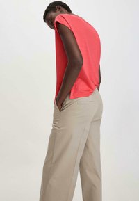 Koraalkleurig T-shirt met korte mouwen en een ruime pasvorm, gecombineerd met lichtbeige broek met wijde pijpen, voorzien van zijzakken en subtiele stiksels.