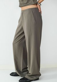 Spodnie o szerokich nogawkach w oliwkowym kolorze w pionowe paski. Wykonane z gładkiego materiału, posiadają boczne kieszenie oraz wygodny elastyczny pasek w talii.