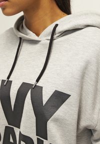 Szara bawełniana bluza z kapturem z przednią kieszenią typu kangur, czarnymi sznurkami oraz dużym czarnym napisem. Miękka faktura i luźny krój.