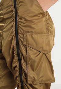Khaki cargobroek van glanzend, lichtgewicht materiaal met een textuurafwerking, voorzien van zijritsen en grote patchzakken.