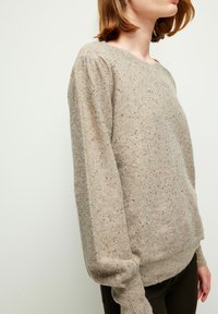 Beige gestrickter Pullover mit strukturiertem Oberflächen, der dezente goldene Sprenkel aufweist, lange Ärmel mit gerippten Bündchen und einem runden Halsausschnitt.