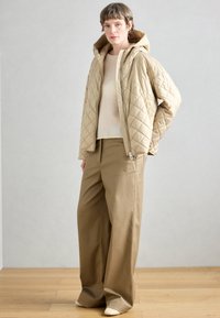 Μπεζ μπουφάν με καπιτονέ σχέδιο και κουκούλα, συνδυασμένο με ανοιχτόχρωμο πλεκτό τοπ και άνετο, ψηλόμεσο παντελόνι σε καφέ απόχρωση. Λεία υφή, μινιμαλιστικός σχεδιασμός.