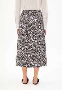 Schwarz-weißer gemusterter Midi-Rock mit elastischem Bund, glatter Textur und fließendem Design, kombiniert mit schwarzen Sandalen.