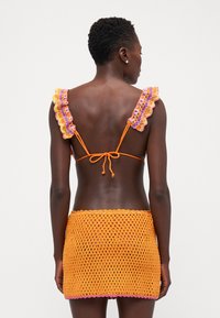 Conjunto de bikini de ganchillo con base naranja, hombros rizados en púrpura y rosa, falda cubriendo de color naranja a juego con diseño de malla texturizada.