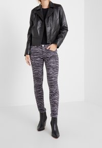 Chaqueta de cuero negra corta, top negro ajustado y jeans pitillo gris con estampado de cebra, combinados con botas negras hasta el tobillo.