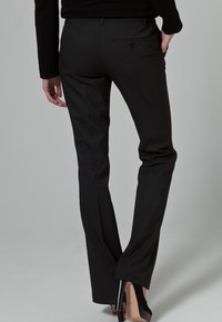 Černé kalhoty na míru s hladkou texturou, slim fit a decentním detailem zadní kapsy, doplněné černými lodičkami na vysokém podpatku.