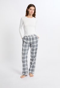 Weißes, geripptes Longsleeve-Shirt kombiniert mit karierten Schlafanzughosen in Blau, Schwarz und Weiß, mit elastischem Bund und Taschen.