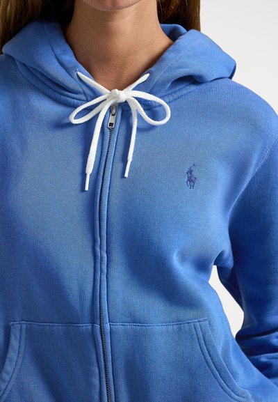 Sweatshirt azul com fecho de correr, feita de mistura de algodão, apresentando um fecho frontal, cordões brancos e um pequeno logótipo bordado no peito.