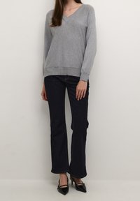 Pull gris à col en V avec poignets et ourlet côtelés, associé à un jean évasé bleu foncé. Le mannequin porte des talons noirs à bout pointu.