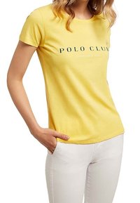 Żółta bawełniana koszulka z okrągłym dekoltem i krótkimi rękawami. Na przodzie ciemnozielony nadruk z napisem "POLO CLUB" oraz "ESTABLISHED 1983".
