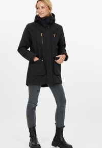 Sort vandtæt parka med hætte, flere lynlåslommer, justerbare manchetter og kontrasterende orange detaljer på lynlåse.