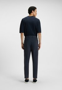 Granatowa koszulka z krótkim rękawem w połączeniu z ciemnymi spodniami, charakteryzująca się luźnym krojem i subtelną fakturą. Czarne trampki dopełniają stylizację.