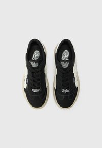 Svart sneakers med hvite og beige detaljer. Laget av stoff og gummi, med en teksturert overflate, rund tå og snøring foran.