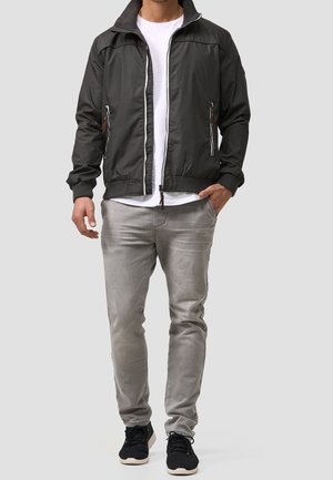 Black jacket with gray accents, zippered front, and side pockets. Paired with a white t-shirt, gray jeans, and black sneakers.