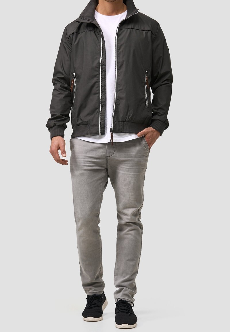 Zwarte jas met grijze accenten, ritssluiting aan de voorkant en zijzakken. Gecombineerd met een wit T-shirt, grijze spijkerbroek en zwarte sneakers.